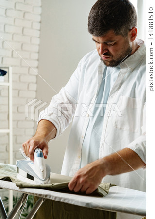 Man ironing clothes at home while preparing for a productive day ahead in a bright room Man ironing clothes at home while preparing for a productive day ahead in a bright room 131881510