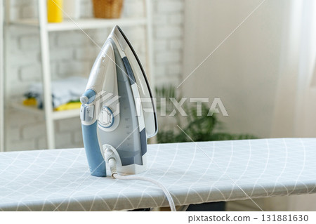 Modern steam iron positioned on an ironing board in a bright room Modern steam iron positioned on an ironing board in a bright room 131881630