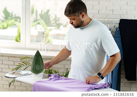 Man ironing a purple shirt in a modern, bright laundry space during the day 131881638