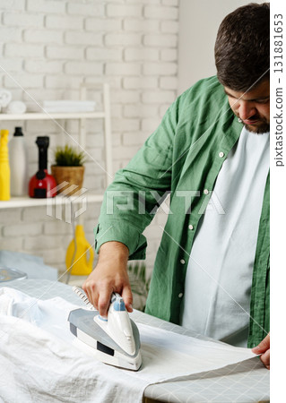 Man ironing clothes in a bright room with modern decor during the daytime Man ironing clothes in a bright room with modern decor during the daytime 131881653