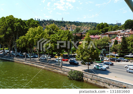 City view along the river showcasing greenery, residential buildings, and urban traffic on a sunny day City view along the river showcasing greenery, residential buildings, and urban traffic on a sunny day 131881660