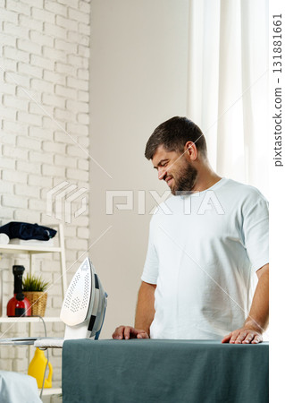 Man ironing clothes in a bright and modern laundry room during the day Man ironing clothes in a bright and modern laundry room during the day 131881661