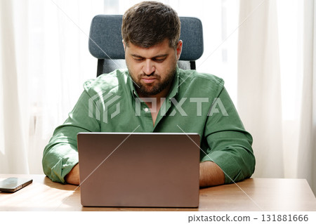 Focused man working on laptop in a well-lit home office Focused man working on laptop in a well-lit home office 131881666