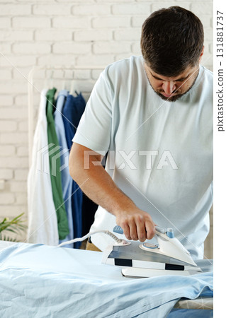 Man ironing a blue shirt in a well-lit laundry room during daytime Man ironing a blue shirt in a well-lit laundry room during daytime 131881737