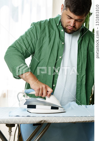 Man ironing a light blue shirt indoors in a cozy living room during the day Man ironing a light blue shirt indoors in a cozy living room during the day 131881810