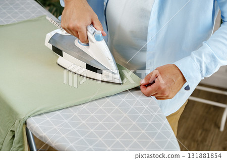 Person ironing a green shirt at home while preparing for the day ahead 131881854