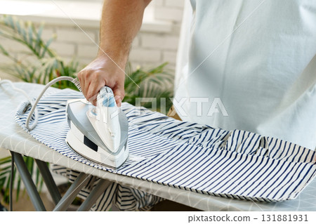 Ironing a striped shirt at home during daylight hours in a cozy indoor setting Ironing a striped shirt at home during daylight hours in a cozy indoor setting 131881931