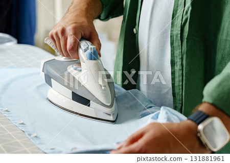 Ironing a blue shirt on an ironing board in a well-lit laundry room 131881961