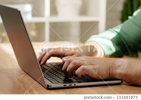 Person typing on laptop while sitting at wooden table in a bright indoor space Person typing on laptop while sitting at wooden table in a bright indoor space 131881973