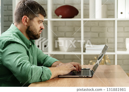 Focused man working on laptop at a desk in a cozy indoor space during daytime 131881981