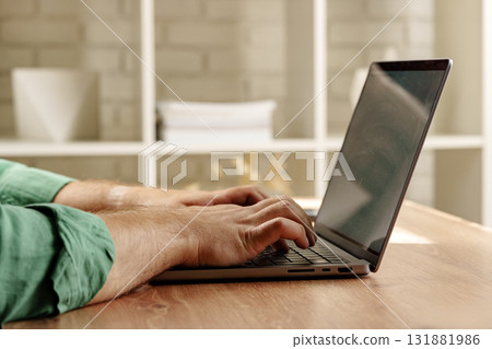 Person typing on a laptop at a wooden desk in a bright indoor space during daytime 131881986