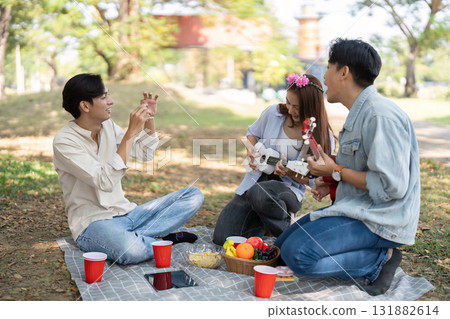 Outdoor Fun and Music Bonding. Friends enjoying a delightful picnic with ukuleles and snacks. Outdoor Fun and Music Bonding. Friends enjoying a delightful picnic with ukuleles and snacks. 131882614