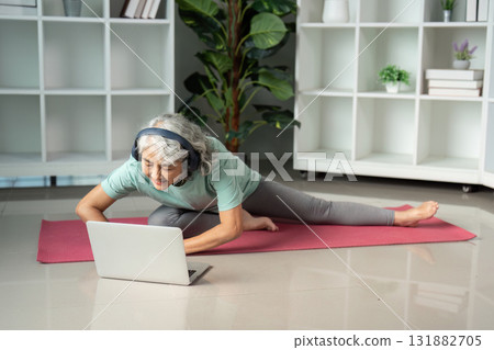 Yoga and Mindfulness. A senior woman engaged in a virtual yoga session, focused on her stretching technique. Yoga and Mindfulness. A senior woman engaged in a virtual yoga session, focused on her stretching technique. 131882705