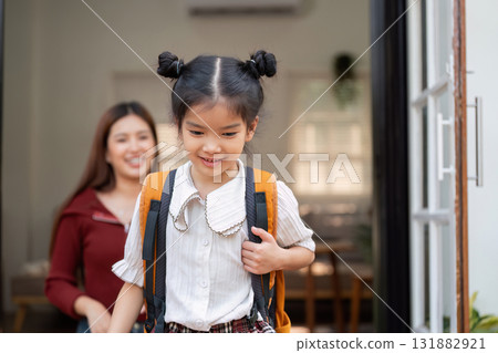 Exciting School Departure. A girl steps out happily with her mother behind her as she heads to school. Exciting School Departure. A girl steps out happily with her mother behind her as she heads to school. 131882921