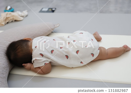Full-body image of a Japanese baby sleeping face down next to a nursing cushion 131882987