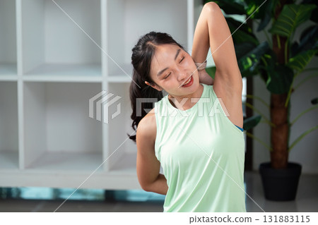 Wellness and Stretching. A woman practicing a shoulder stretch in a serene home environment. 131883115