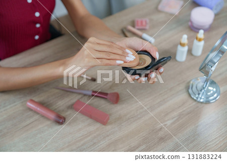 Makeup Application with Products. A woman applying foundation from a compact surrounded by various beauty products. Makeup Application with Products. A woman applying foundation from a compact surrounded by various beauty products. 131883224