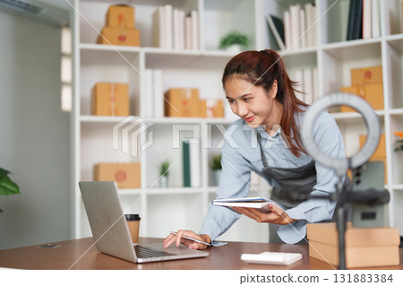 Entrepreneurship and E-commerce. A female entrepreneur managing online sales with a laptop and notebook. 131883384
