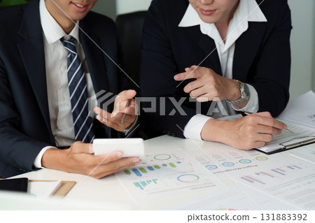 Strategic Planning and Data Review. Business partners discussing analytics on a mobile device, focusing on key performance indicators. 131883392