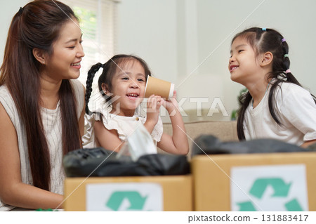 Joyful Moments and Eco Awareness. A mother and her two daughters share a playful moment, creatively engaging with recycled materials. 131883417