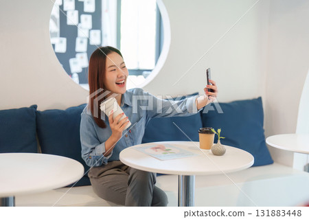 Connection and Sustainability. A joyful woman enjoying her coffee while taking a selfie in a modern cafe setting. Connection and Sustainability. A joyful woman enjoying her coffee while taking a selfie in a modern cafe setting. 131883448