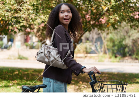Eco-Conscious Commuting and Stylish Lifestyle. A woman with her bicycle smiling in a natural setting, advocating for a sustainable way to travel. 131883451
