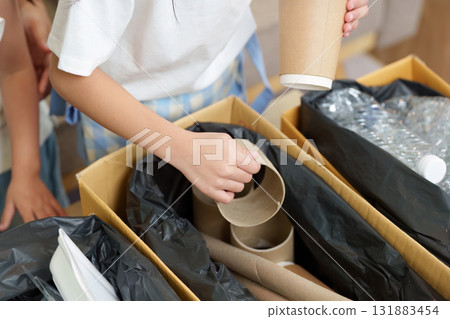 Eco-consciousness and Family Engagement. A child actively participates in a recycling task, organizing cardboard items for environmental responsibility. 131883454