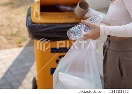 Promoting recycling habits. A woman holds a plastic bottle and a bag while preparing to recycle in an outdoor setting. Promoting recycling habits. A woman holds a plastic bottle and a bag while preparing to recycle in an outdoor setting. 131883522