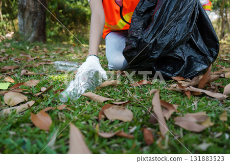 Promoting Eco-Consciousness. A volunteer diligently collects plastic bottles from the grass during a park cleanup campaign. Promoting Eco-Consciousness. A volunteer diligently collects plastic bottles from the grass during a park cleanup campaign. 131883523