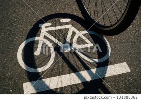 Bicycle wheel casting shadow over painted cycling lane symbol on sunlit urban asphalt street, promoting eco friendly transportation, AI Generative 131885362