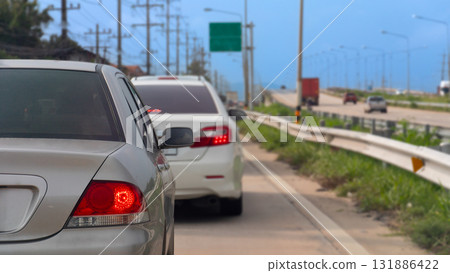 Rear side of luxury car with turn on brake light. Beside with guardrail and green grass. Separation of main and side traffic routes. Clear traffic conditions. Rear side of luxury car with turn on brake light. Beside with guardrail and green grass. Separation of main and side traffic routes. Clear traffic conditions. 131886422