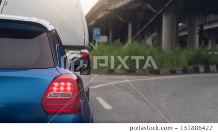 Rear side of mini car blue color with turn on brake light. Parking behind a cargo car. Side of car with curved asphalt road for U-Turn under level bridge. 131886427