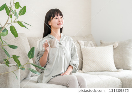 一位輕鬆的亞洲女性，早上在家用杯子喝茶和熱水（Onkatsu） 131889875