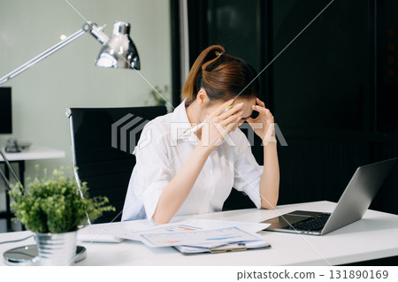 Asian woman feeling migraine head strain.Overworked businesswoman financier while working on laptop and tablet Asian woman feeling migraine head strain.Overworked businesswoman financier while working on laptop and tablet 131890169