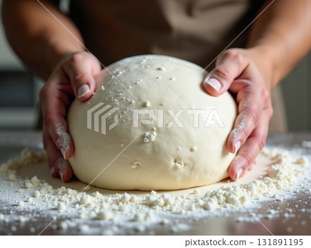 Extreme close-up of a baker's hands gently supporting a perfectly smooth, rising dough ball dusted with white flour on a dark table. Extreme close-up of a baker's hands gently supporting a perfectly smooth, rising dough ball dusted with white flour on a dark table. 131891195