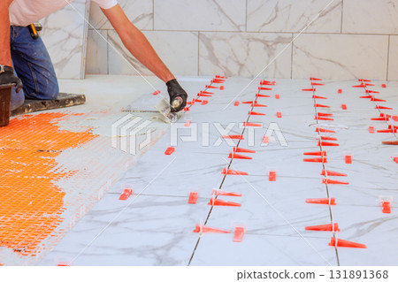 Worker applies adhesive arranges tiles with clips for precise spacing clean finish. 131891368