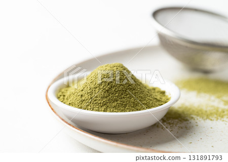 Matcha green tea powder in bowl and sieve on plate with white background 131891793