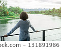 Woman standing on outdoor balcony overlooking peaceful river and mountain view, eco resort escape for digital detox, nature connection, and mental health wellness in sustainable travel. 131891986