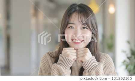 A young woman wearing a sweater smiling and making a small fist pump 131892160
