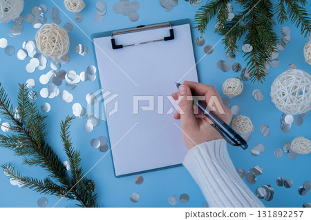 Female hands in white cozy sweater writing on empty white paper notepad on blue background. Preparation for New Year or Christmas. Copy space mock up planning and setting goals for personal Female hands in white cozy sweater writing on empty white paper notepad on blue background. Preparation for New Year or Christmas. Copy space mock up planning and setting goals for personal 131892257