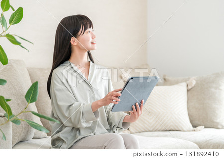 年輕的亞洲女性坐在沙發上使用平板電腦 年輕的亞洲女性坐在沙發上使用平板電腦 131892410