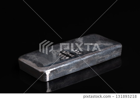 Silver bar on a glass plate, against black background. Stamped cast silver ingot, of one kilogram, about 32 troy oz of metal, with a purity of 999.0, that is 99.9 percent pure silver. Side view. Photo 131893218