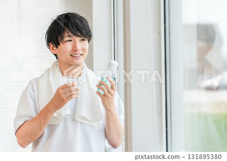 A young Asian man taking care of his bad breath by using mouthwash in the morning 131895380
