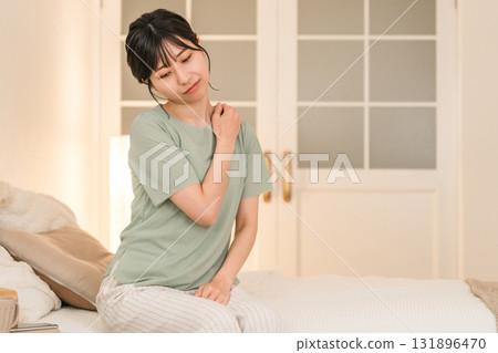 Young Asian woman suffering from stiff shoulders in her bedroom at night Young Asian woman suffering from stiff shoulders in her bedroom at night 131896470