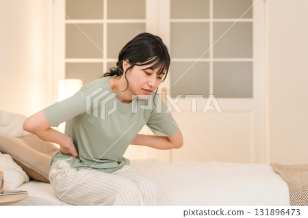 Young Asian woman suffering from abdominal pain and menstrual cramps in her bedroom at night Young Asian woman suffering from abdominal pain and menstrual cramps in her bedroom at night 131896473