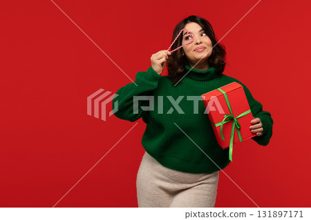 Woman holding gift box and candy cane heart near eye Woman holding gift box and candy cane heart near eye 131897171