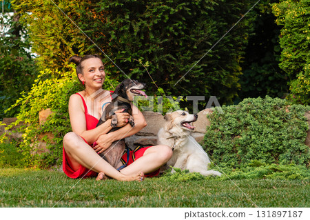 Woman in red dress sitting with two dogs in garden Woman in red dress sitting with two dogs in garden 131897187