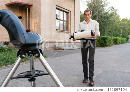 Astronomer carrying telescope tube toward tripod setup 131897194