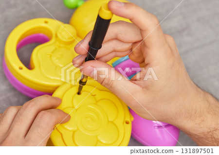 male hands with screwdriver repairing kids toy on grey table. repair shop male hands with screwdriver repairing kids toy on grey table. repair shop 131897501