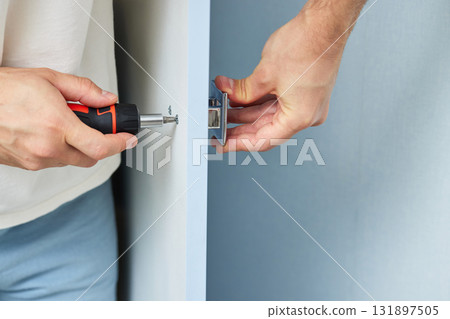 worker installing new handle of cabinet door with screwdriver, close-up. furniture assembly service 131897505